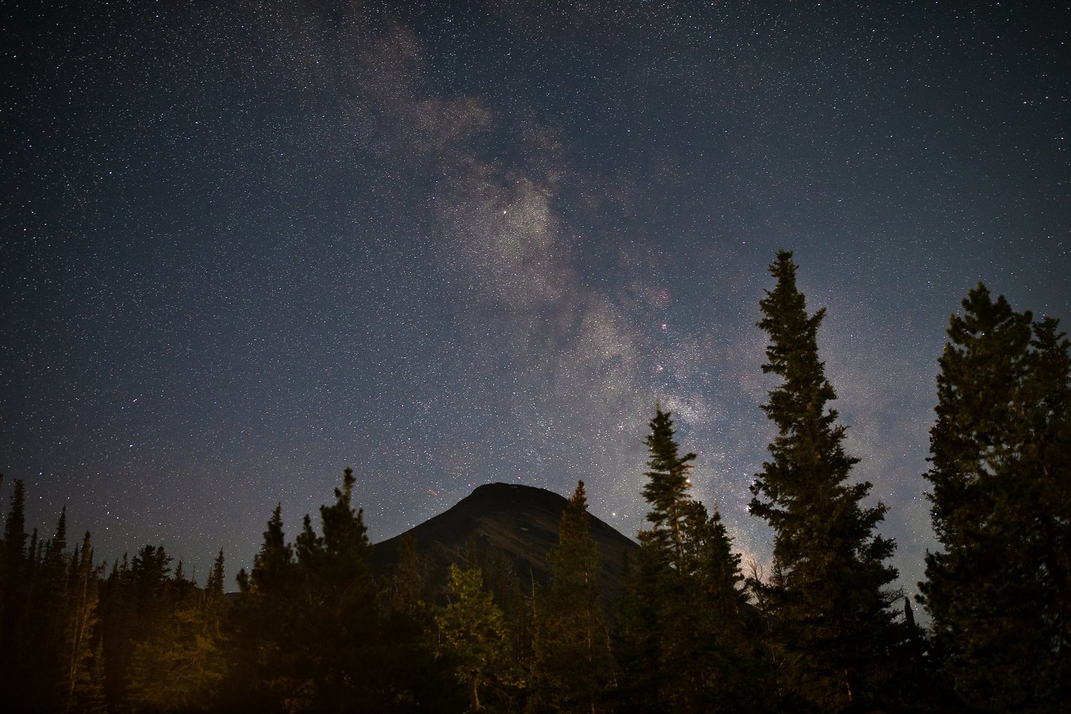 Stars above a dark forest and distant mountain