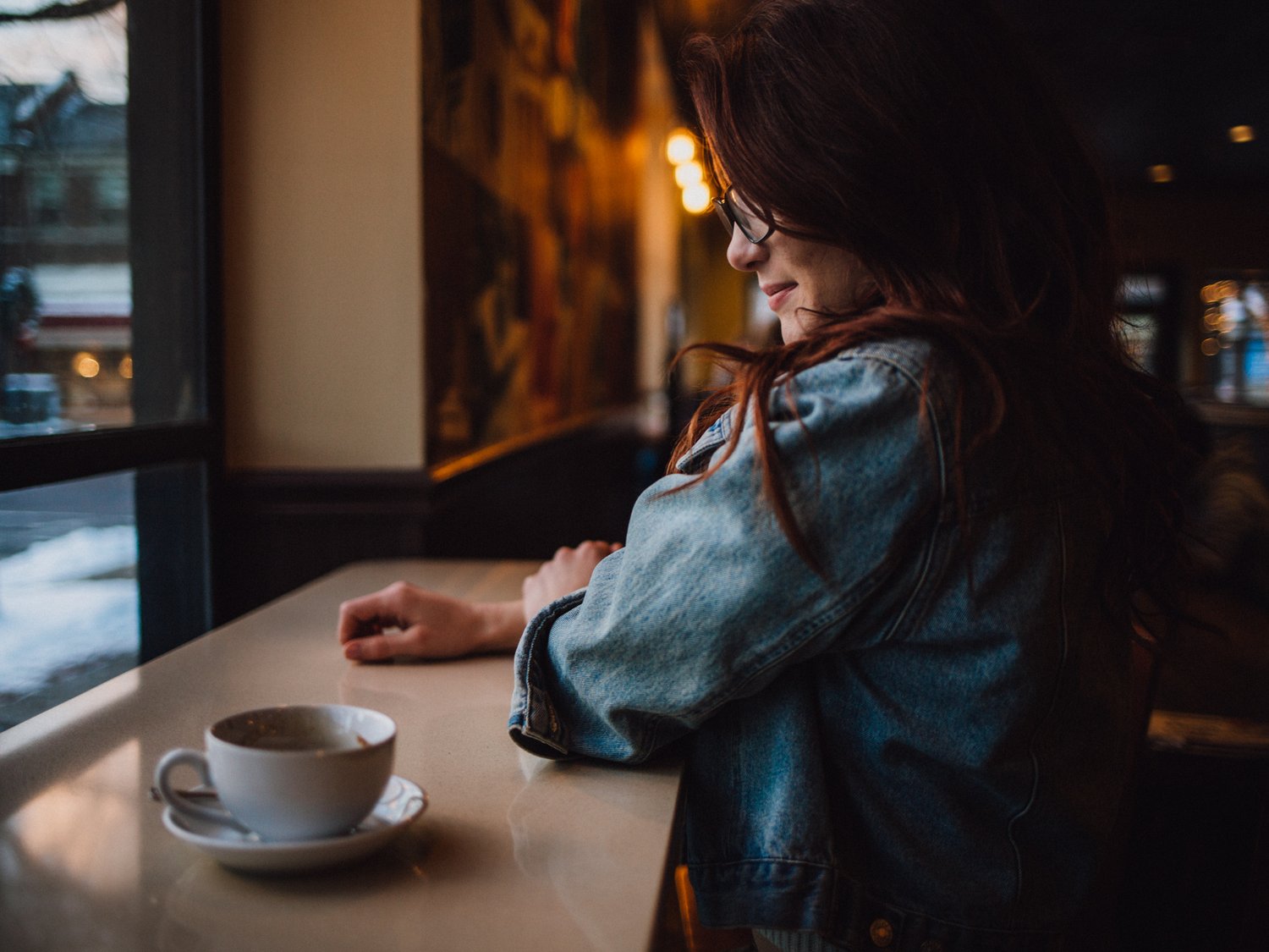 Woman at a cafe table looking toward a window